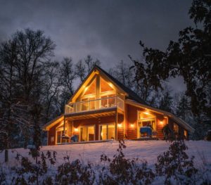 A well lit home at dusk with snow around it